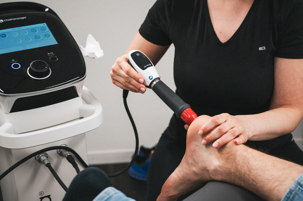 Therapeutin behandelt einen Fuß mit einem Chattanooga-Stosswellentherapiegerät